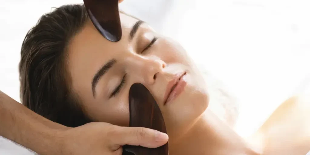 A Client With Closed Eyes Receives A Gua Sha Facial Treatment At Serenity Head Spa