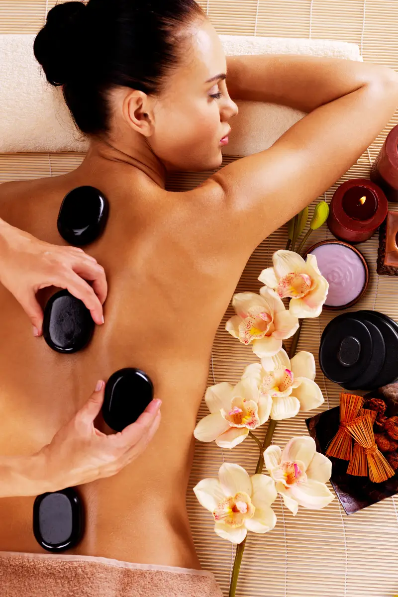 Hot stone massage being performed on a woman's back, with a masseur placing the stones.