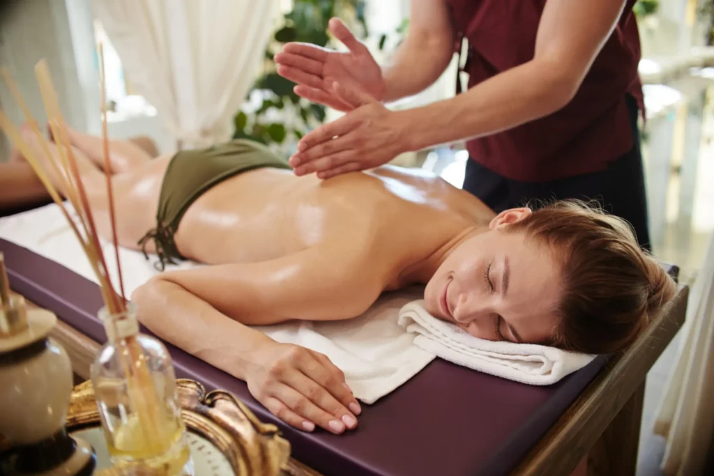 A Relaxing Spa Scene With A Woman Receiving A Back Massage On A Massage Table, With Decorative Items In The Foreground.
