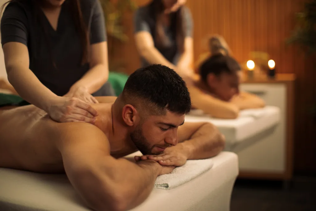 A couple lies side-by-side on massage tables in a serene spa setting, enjoying a couples massage. This shared experience can be a way to relax together and strengthen their relationship.