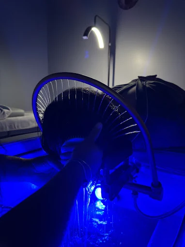 A person's hair is being washed under a blue light, with a curved piece of equipment over their head.