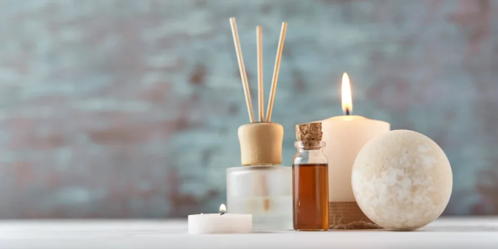 Lymphatic Drainage Massage For Stomach Bloating: Benefits &Amp; Guide 3 A Collection Of Spa Products Including A Reed Diffuser, A Small Vial Of Essential Oil, A Lit Candle, And A Bath Bomb Against A Rustic Blue Background