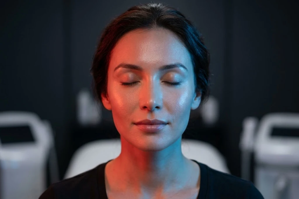 A portrait of a woman with her eyes closed, featuring red and blue light therapy highlights on her face in a professional spa setting.