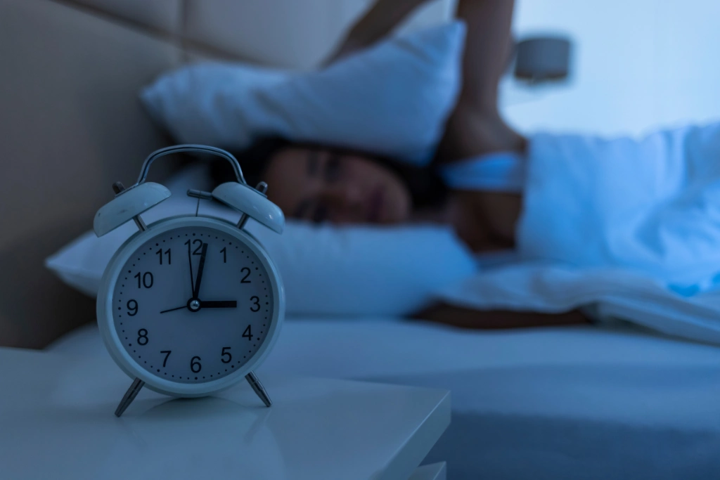 An alarm clock at 3:00 AM with a person awake in bed, showing difficulty sleeping.