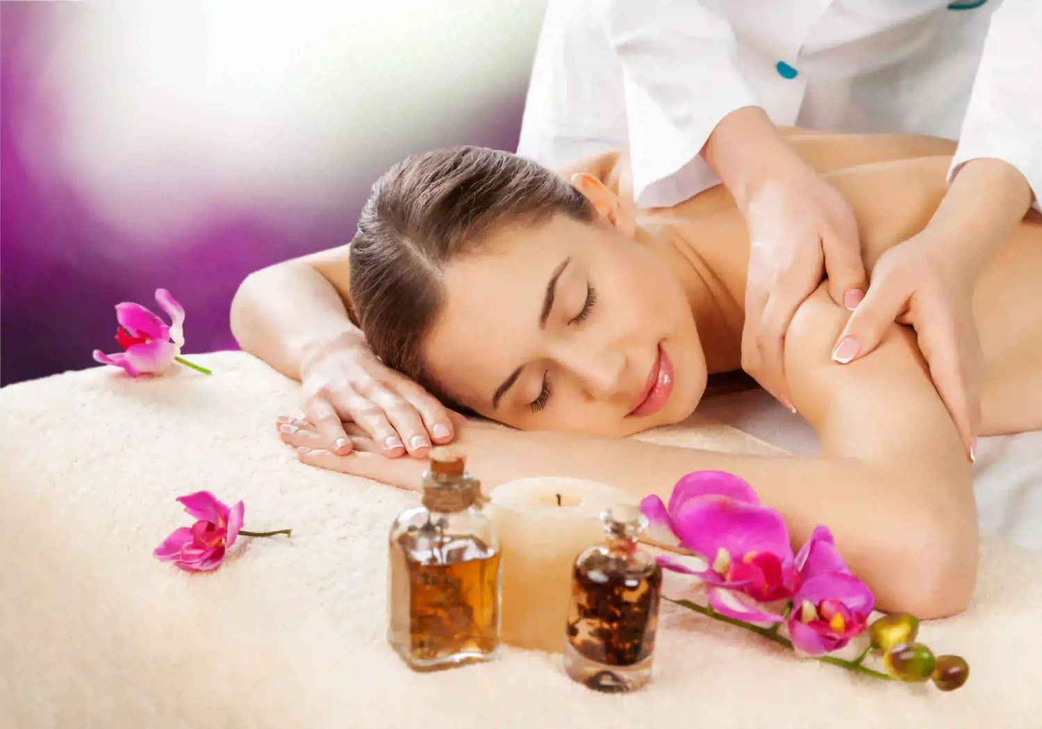 : A Woman Receiving A Professional Full Body Massage At A Spa, Featuring Essential Oils, A Lit Candle, And Pink Orchids On A Massage Table.