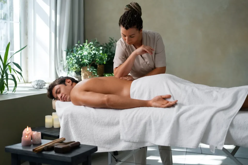 A Professional Massage Therapist Using Her Forearm To Apply Deep Pressure During A Therapeutic Back Massage For A Man At A Wellness Center.