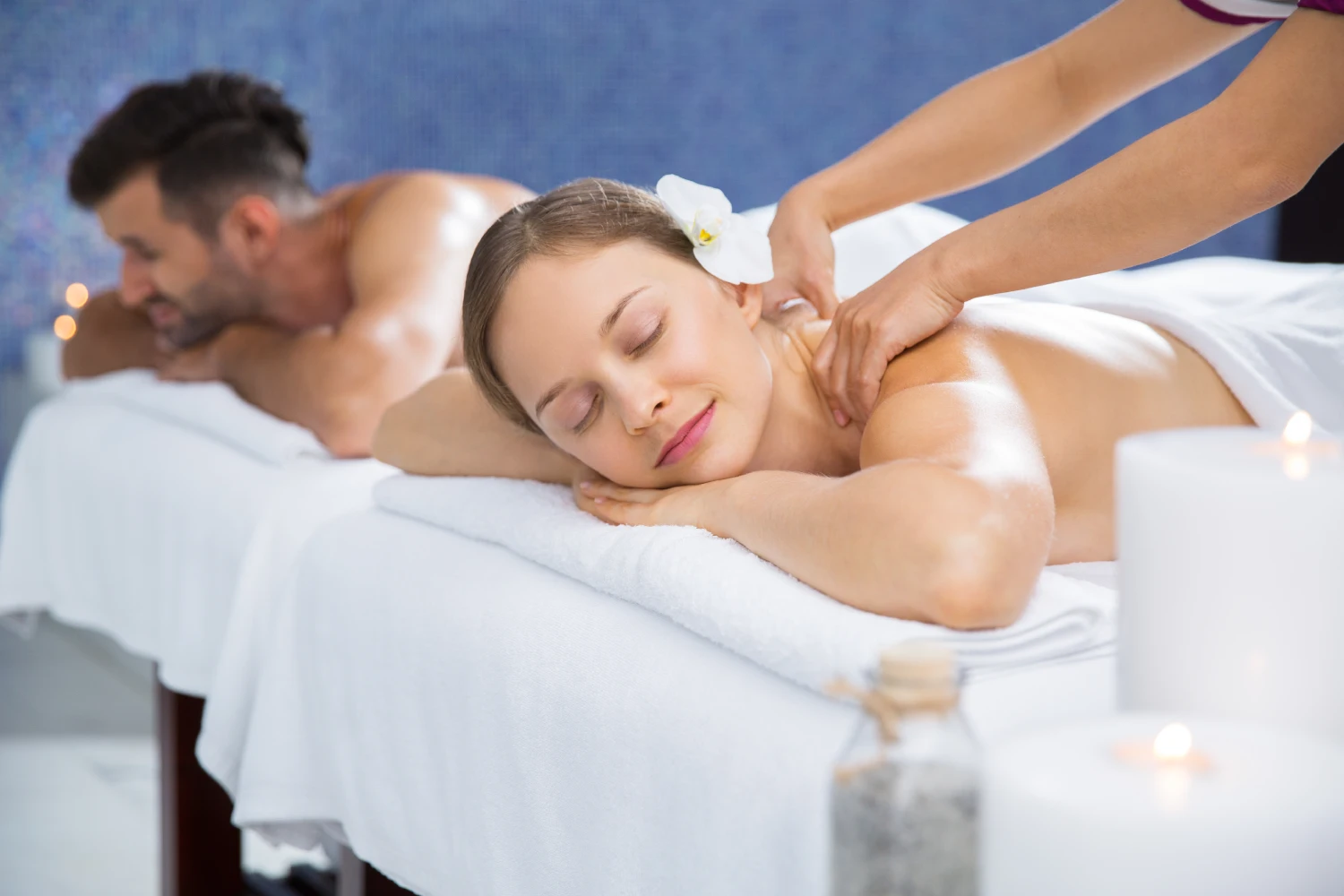 A Man And A Woman Side-By-Side On Massage Tables Receiving A Professional Couple Massage In A Serene Spa Environment.