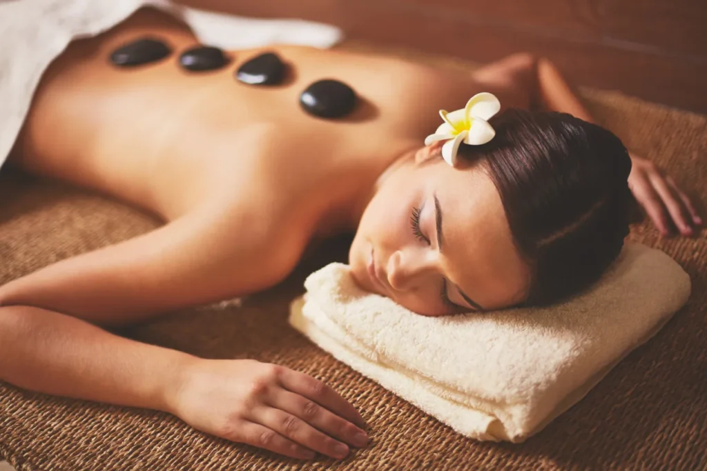A Woman Resting Peacefully During A Professional Hot Stone Massage With Smooth, Heated Basalt Stones Placed Along Her Back In A Warm Spa Setting.