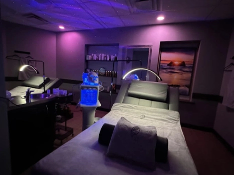A Relaxing Spa Treatment Room With An Adjustable Facial Bed Under Calm Purple Lighting.